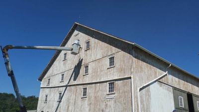 old barn being painted from a bucket truck lift