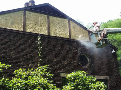 worker pressure washing side of large brick house from a bucket truch