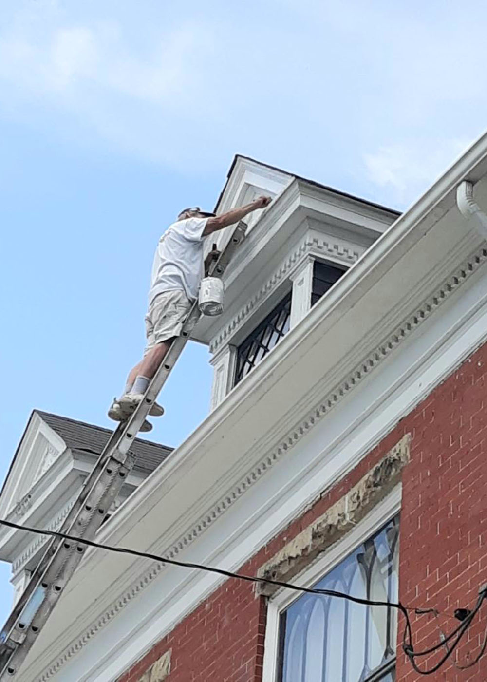 Man painting Victorian house trim on dormer