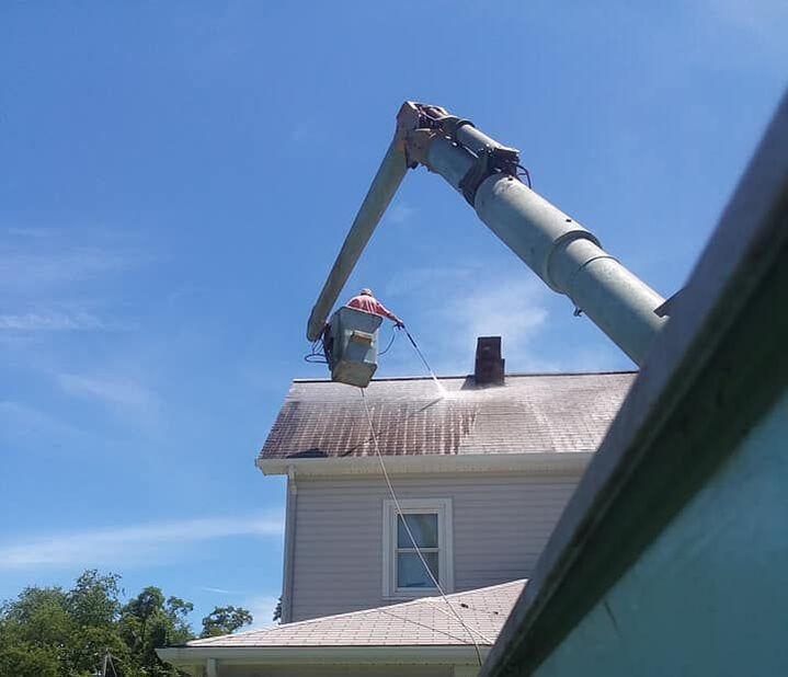 man cleaning asphalt roof from a bucket truck